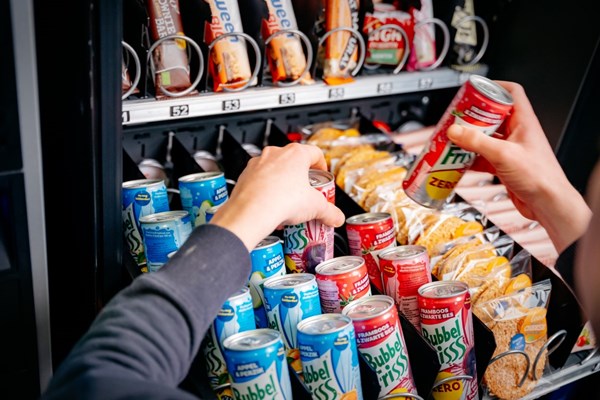 Medewerker van DGA vult de automaat bij met blikjes en snacks